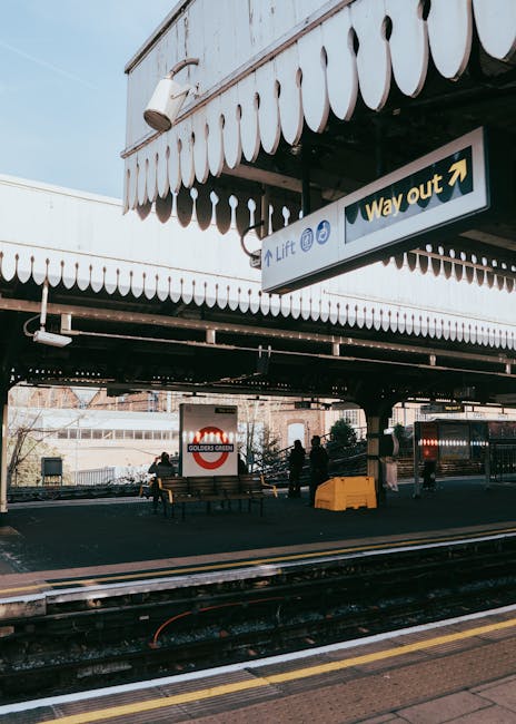 Exterior view of Barnes Cray station with a canopy overhead displaying a sign that reads 'Way out' and an arrow pointing to the right. The platform features several people waiting, some seated on wood